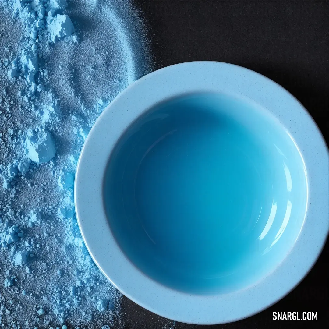 Bowl of blue food is on a table next to a bowl of powdered sugar and a spoon