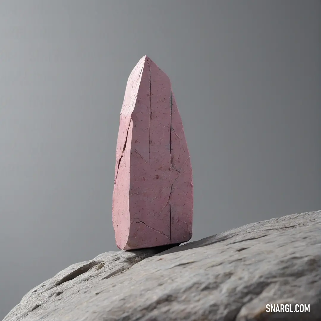 A striking pink rock balances atop a rugged gray boulder, nestled amidst dirt and natural elements under a cloudy sky. The color contrast and textures enrich the scene, inviting exploration of nature's wonders.