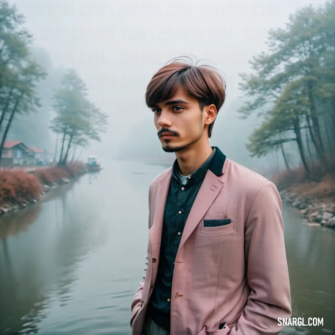 Man standing in front of a body of water wearing a pink suit and black shirt. Color Pale pink.