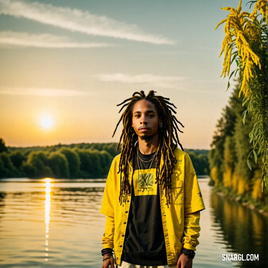 Man with dreadlocks standing in front of a lake at sunset with a yellow jacket on and a black shirt. Example of RGB 249,218,0 color.