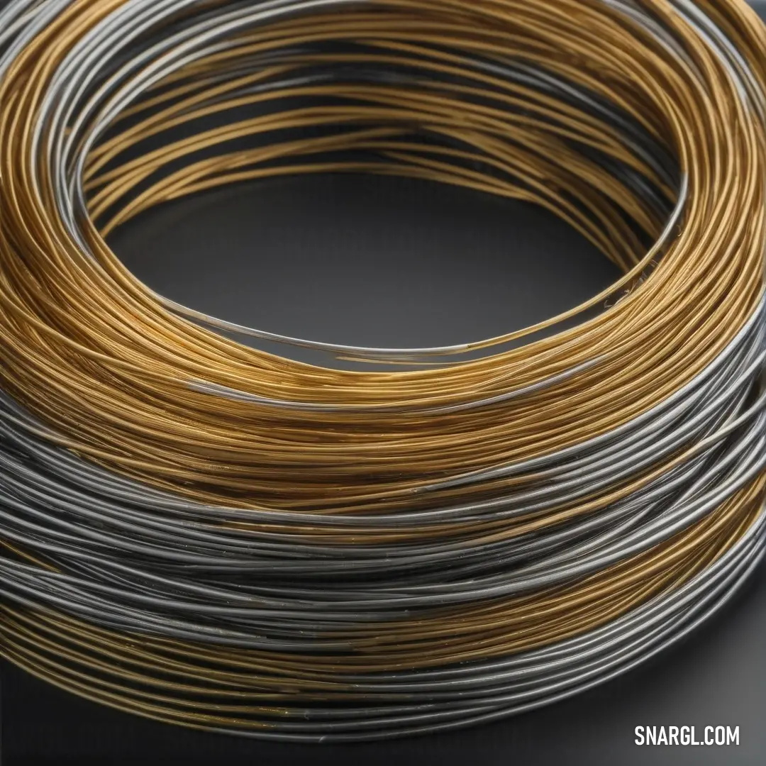 A close-up of a coil of gold and silver wire artistically resting on a dark black surface. The vibrant contrast highlights the blend of colors and textures, creating a visually stunning representation of craftsmanship.