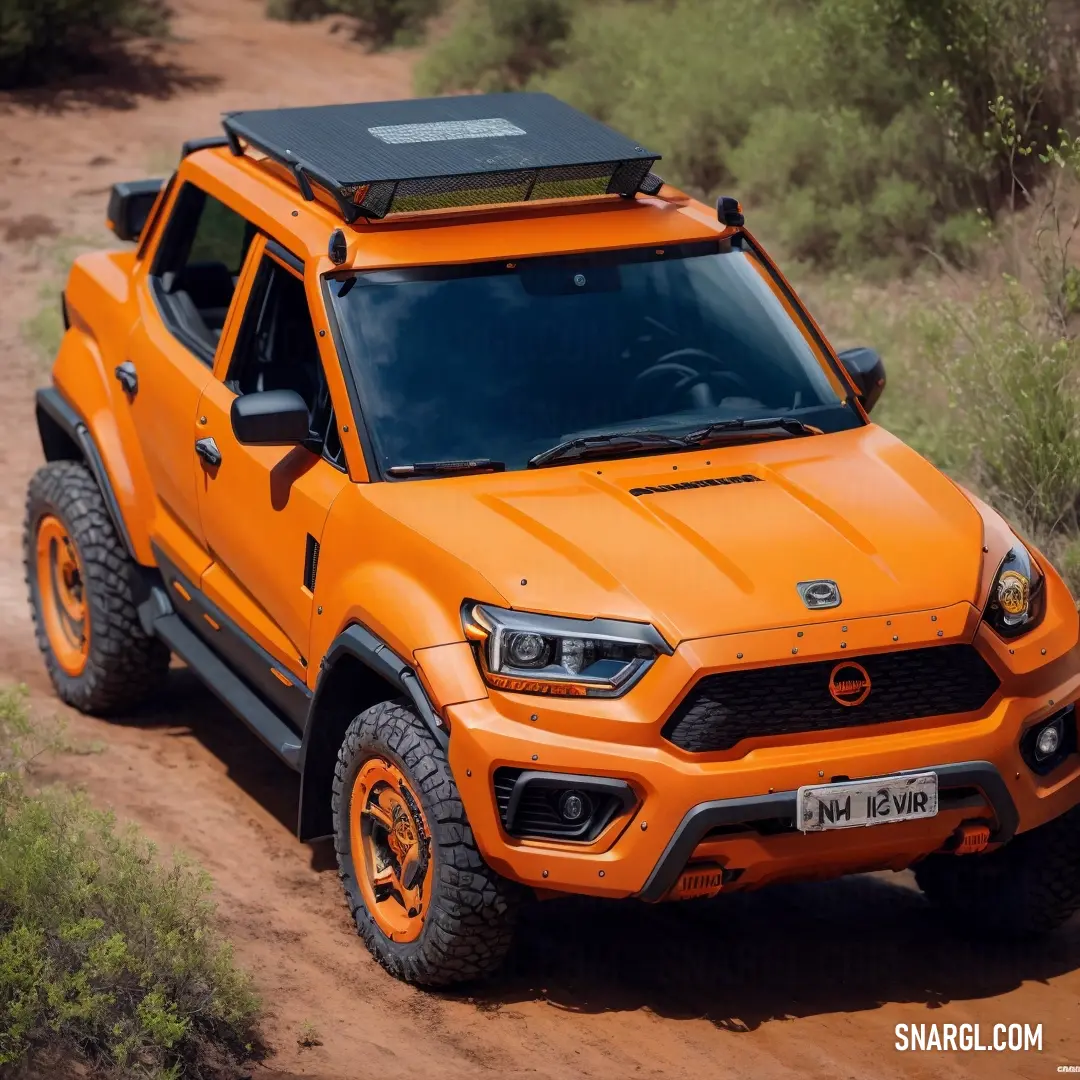 Bright orange truck is driving down a dirt road in the desert with a black roof box on top