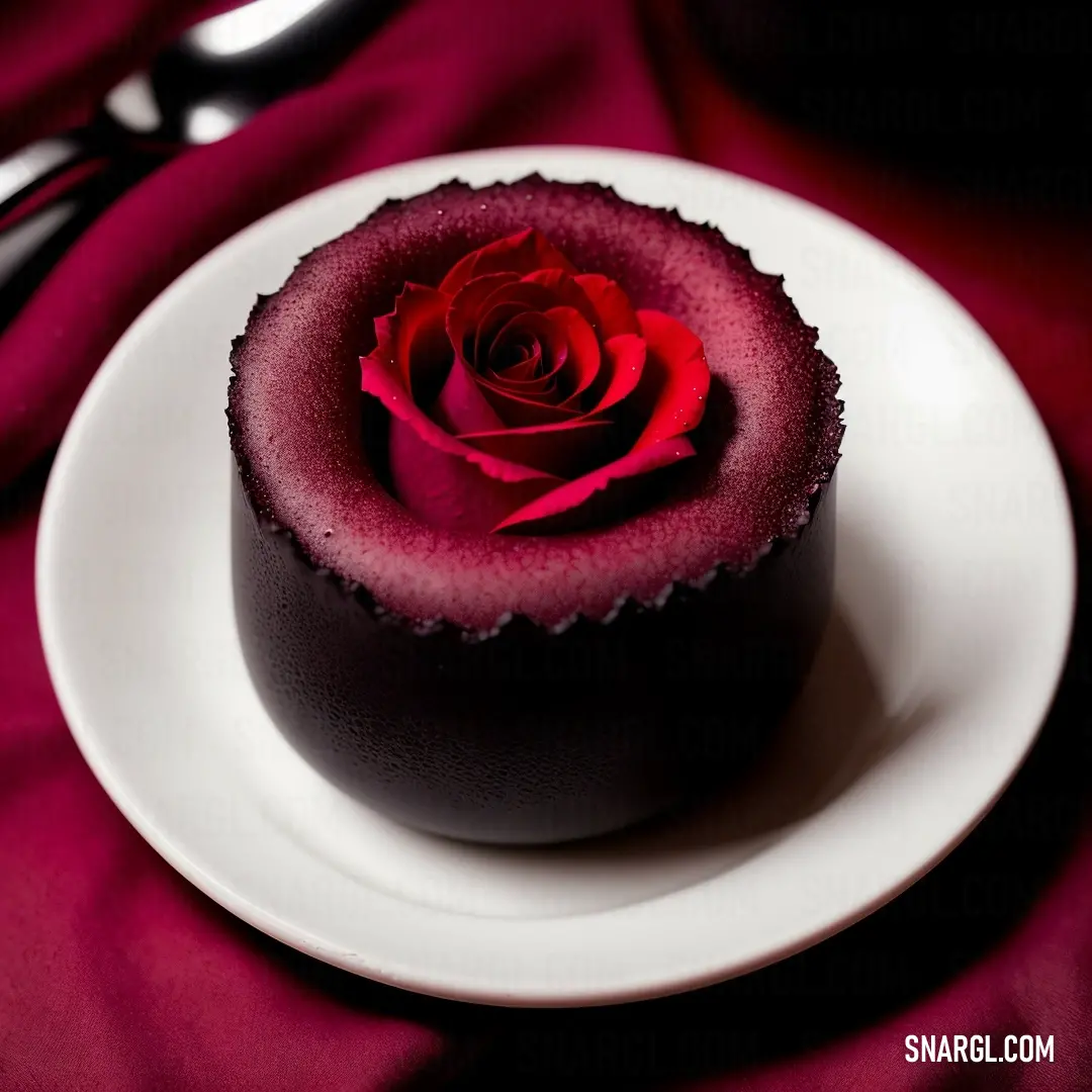 Small chocolate cake with a red rose on top of it on a plate with a fork and spoon. Color PANTONE 1955.