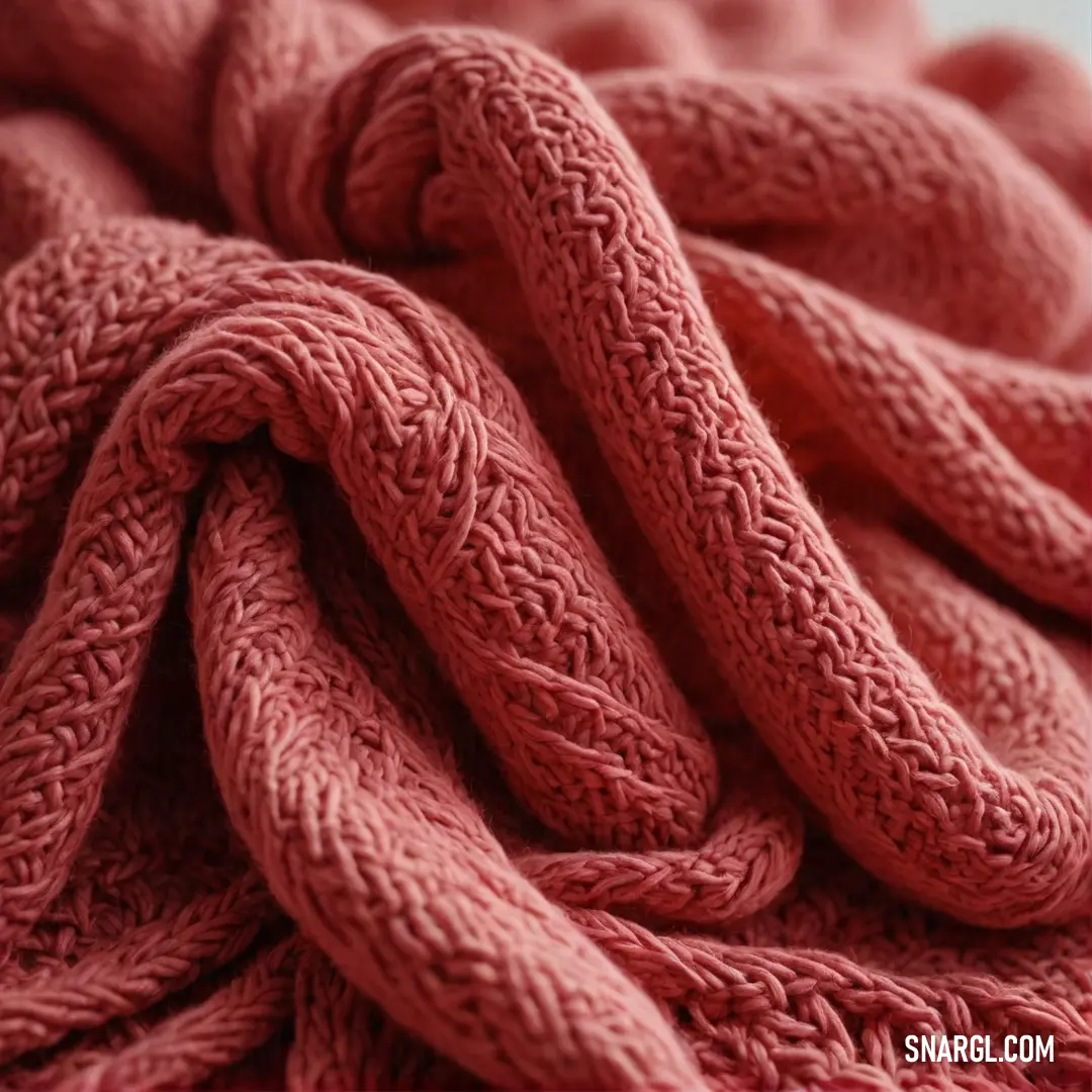 A close-up of a unique blanket featuring a knot detail at one end, paired with a bold red blanket, highlighting the vibrant contrast of colors and textures with an intimate glimpse of warmth and coziness.