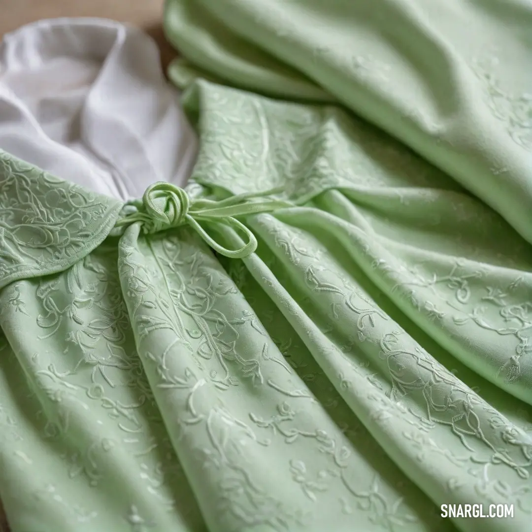 An eye-catching green dress is carefully displayed on a pristine white table, layered with a white shirt underneath and accented by a charming green bow. The serene atmosphere brings forth the delicate #E7C9D2 hue.