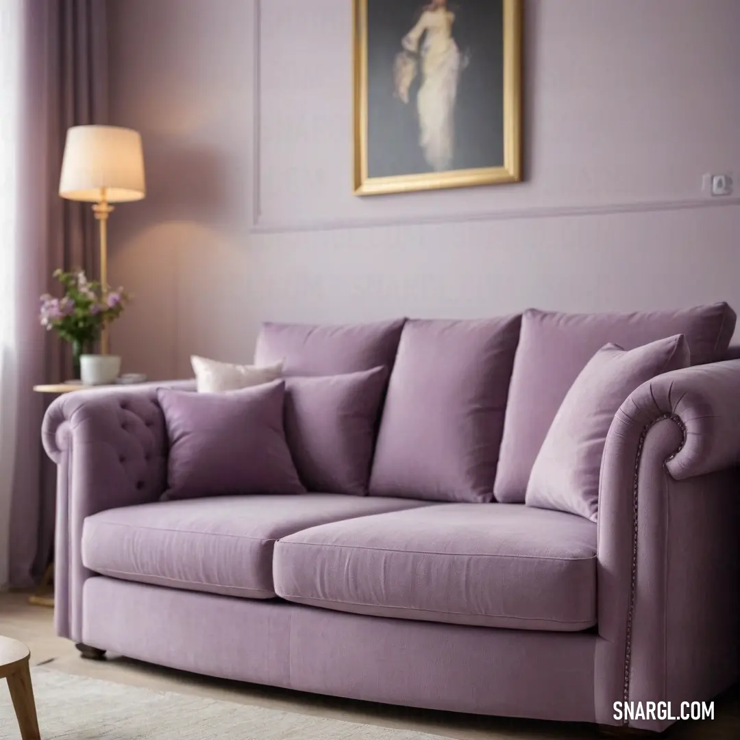 A cozy living room scene features a plush purple couch complemented by a beautiful painting above it. A stylish lamp rests on the table, contributing warmth to the inviting atmosphere of this well-designed space.