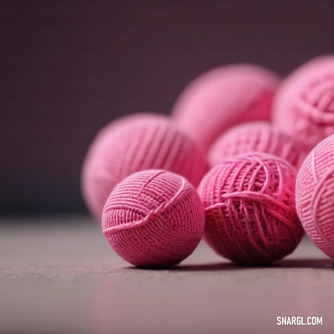 A pile of soft, pink yarn balls sits atop a tabletop, surrounded by a dark background that highlights the subtle richness of color #C16198. The yarn's texture adds warmth to the scene.