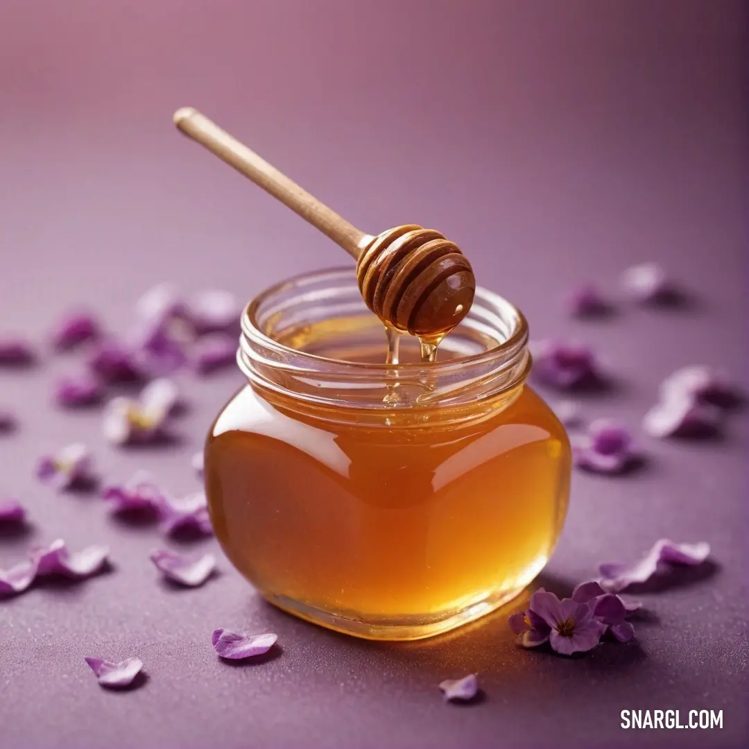 An aesthetically arranged jar of honey glistens amidst a setting of delicate flowers, accompanied by a wooden spoon. The rich hues of purple in the background accentuate the warmth and sweetness of this serene composition.