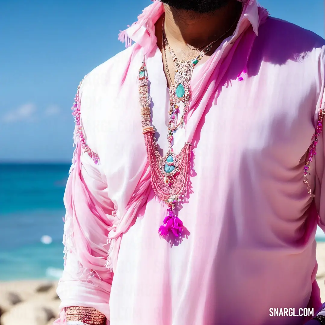 Man wearing a pink shirt and a necklace on the beach with a blue sky in the background