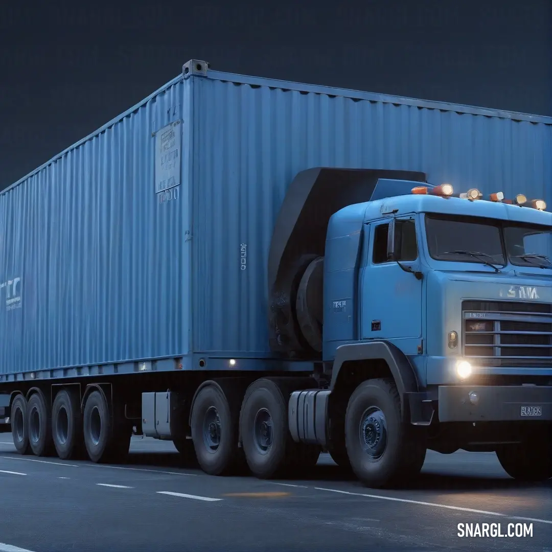 A large blue truck with its headlights on drives down an empty street at night, pulling a trailer behind it. The rich blue color (#00527F) is highlighted by the glow of the lights and the streetlights illuminating the road ahead.