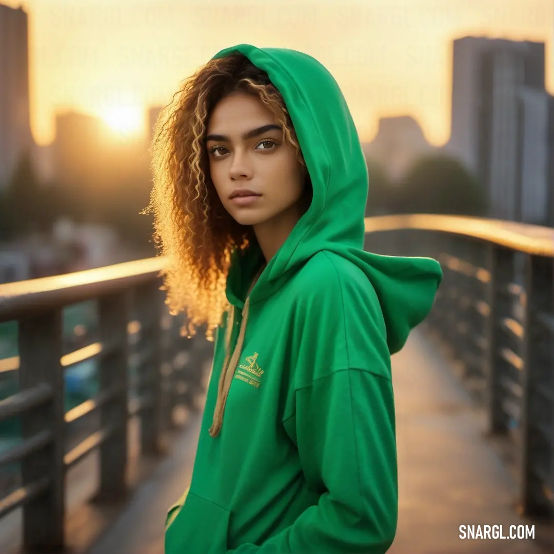 Woman in a green hoodie standing on a bridge with a city skyline in the background. Color #009739.