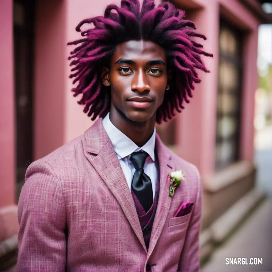 Man with a suit and tie with dreadlocks on his head and a pink wall behind him. Example of CMYK 1,41,0,0 color.
