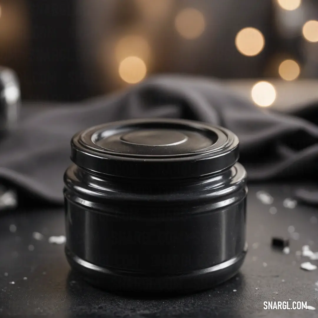 A black jar sits atop a sleek table, contrasting beautifully with a rich black cloth beside it, complemented by a metallic silver object. The blurred background adds an aura of mystery to this intriguing composition, inspired by the color #675A39.