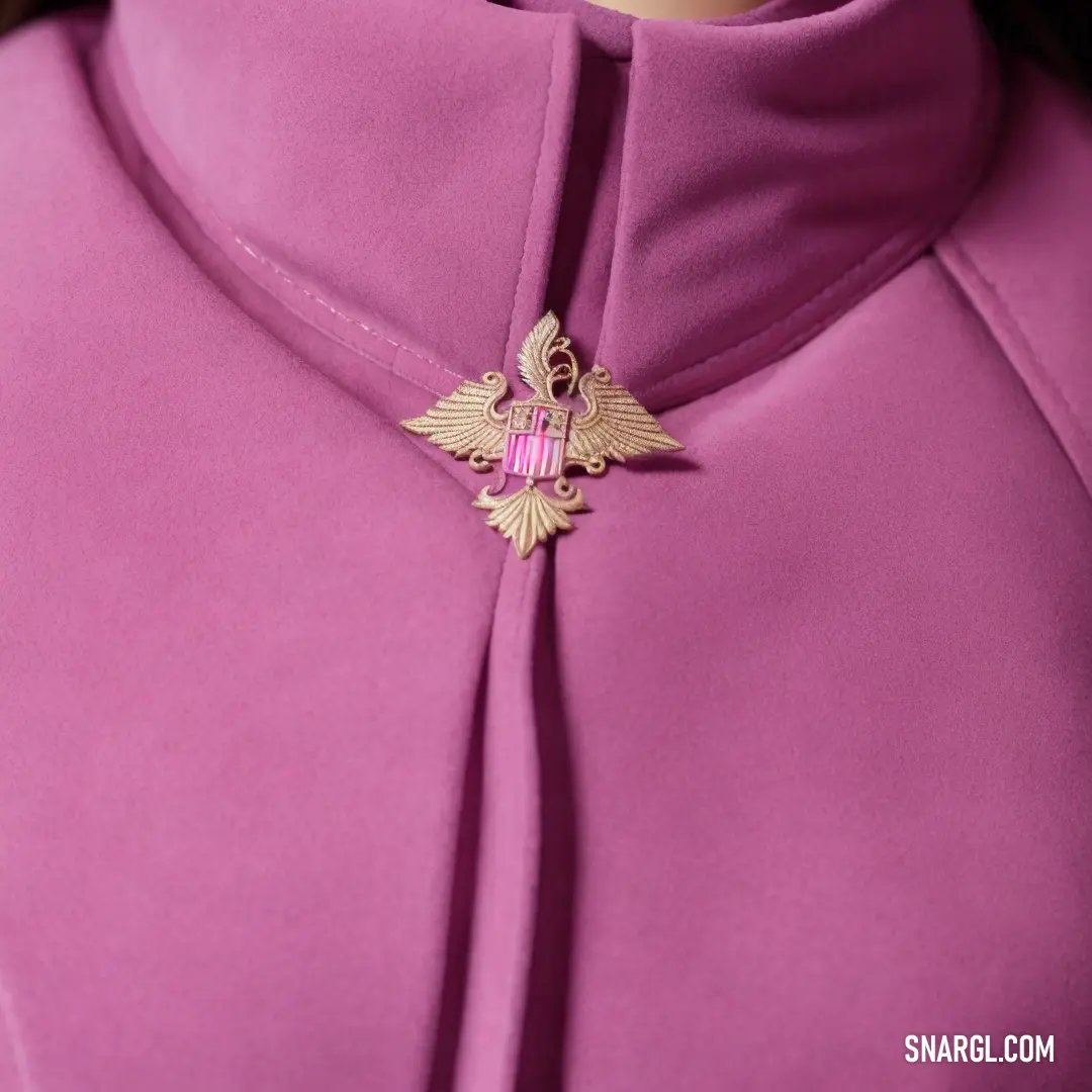 Close up of a woman wearing a pink coat with a gold bird brooch on it's collar. Color CMYK 12,74,0,0.