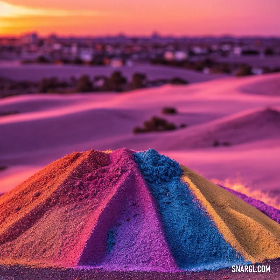 Pile of colorful sand on top of a sandy beach next to a sunset sky and a city