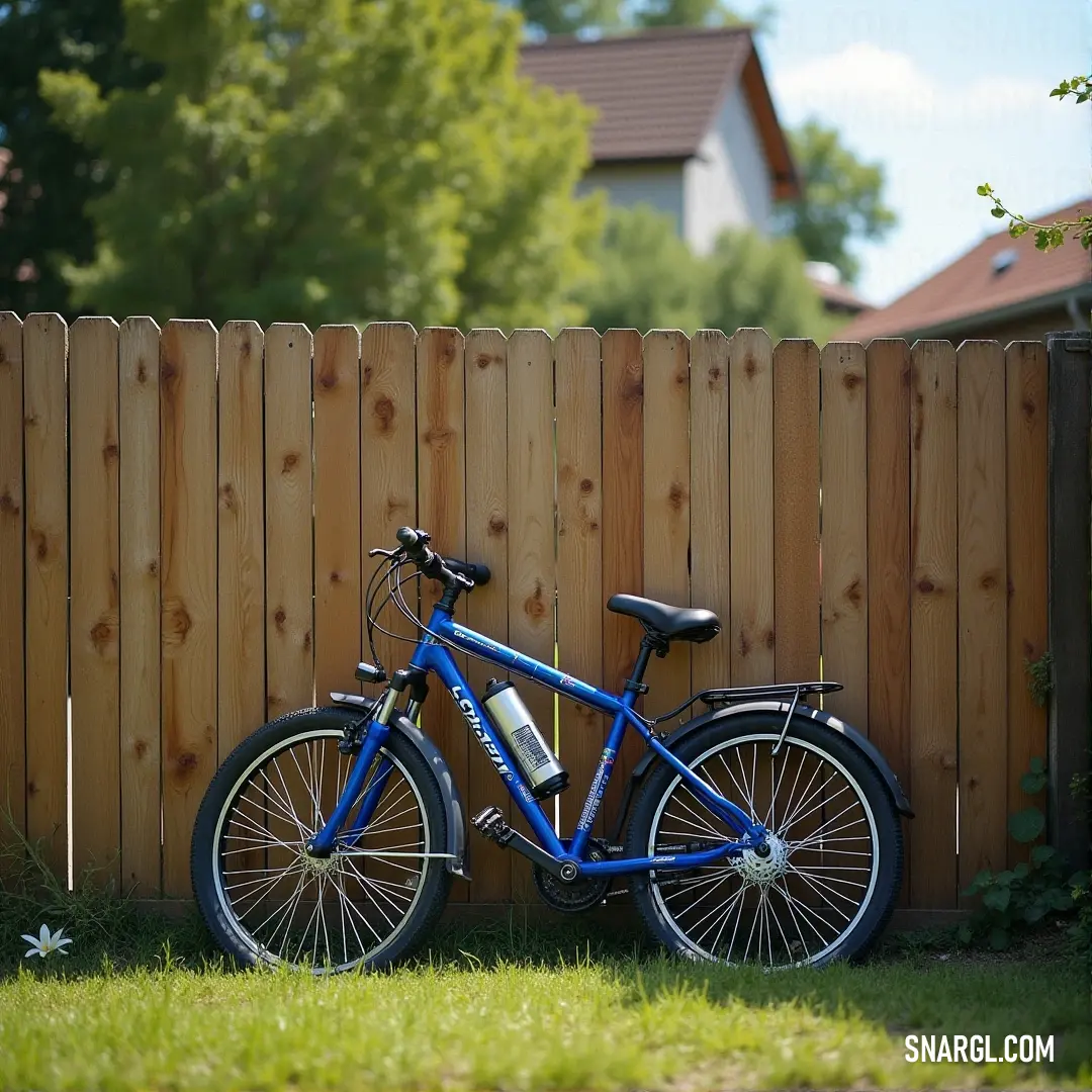 A bright blue bicycle rests peacefully beside a rustic wooden fence, nestled in a serene yard adorned with lush grass and verdant trees, symbolizing carefree summer days.