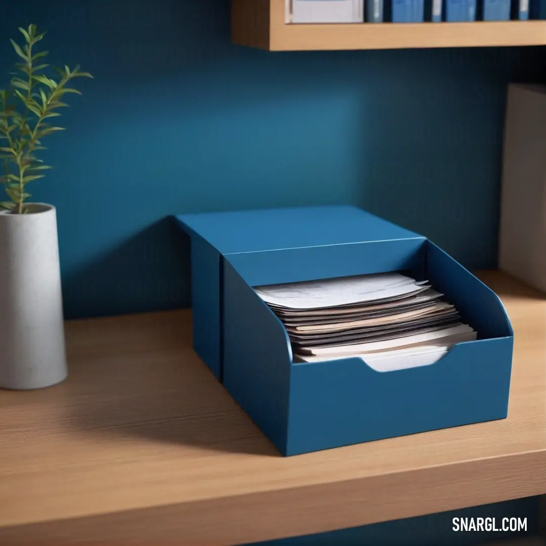 A vibrant blue box filled with neatly stacked papers sits on a desk adorned with a lush plant and an elegant white vase, offering a snapshot of creativity and organization in a charming workspace environment.