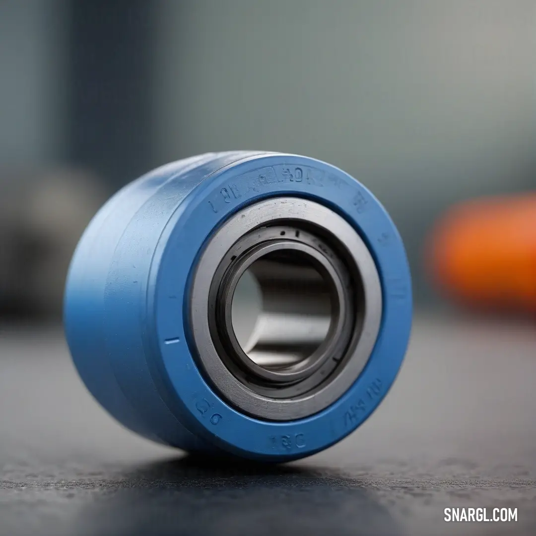 A blue skateboard, featuring a matching blue bearing unit, rests on a table with a bright orange carrot in the background. The vivid contrast of colors makes this image both playful and eye-catching.