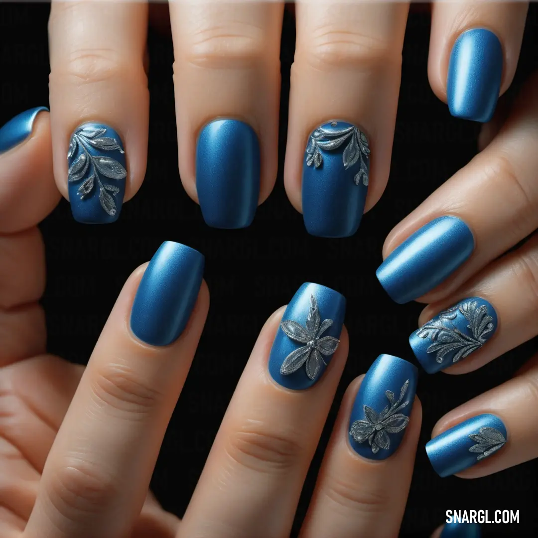 Woman's hands with blue nail polish and a flower design on them, with a black background. Example of #005E98 color.