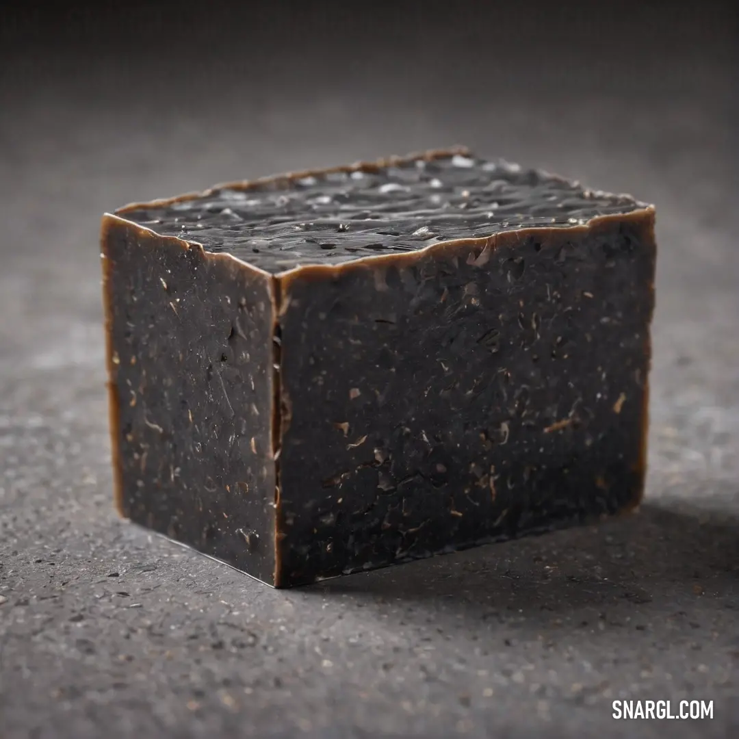 A visually striking square soap bar resting on a sleek gray surface, topped with an intriguing black substance that adds a mysterious allure. This arrangement emphasizes the PANTONE 2965 color principle.