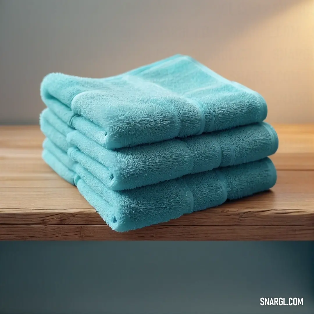 A stack of towels is placed on a rustic wooden table next to a warm lamp with a gentle light. The warm wood and soft lighting create a cozy and inviting atmosphere, enhancing the towels' serene blue color.