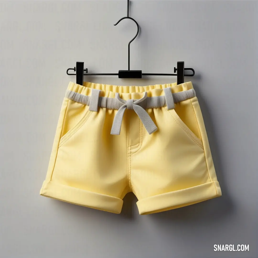 A striking pair of bright yellow shorts hangs gracefully on a wooden hanger against a wall, exuding a cheerful summer vibe. Showcasing a tasteful blend of style and color, these shorts embody the spirit of playful fashion with a CMYK 9,0,66,0 color exampl