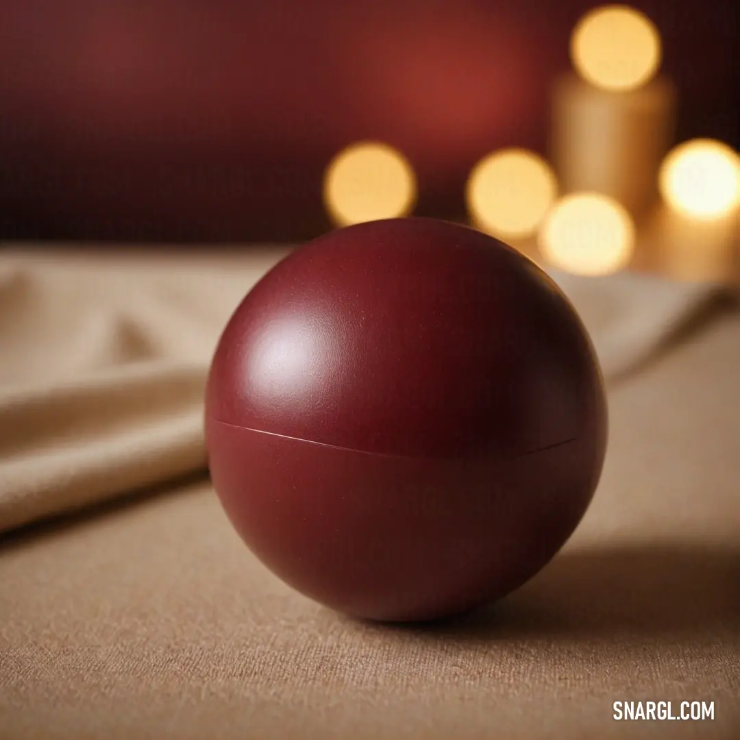 A vibrant red spherical ornament rests gracefully atop a wooden table, accompanied by a delicately designed candle holder and a elegantly draped tablecloth, creating a warm and inviting atmosphere that highlights its PANTONE 4645 color tone.