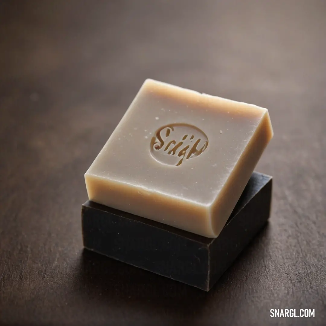 An alluring soap bar adorned with a logo resting on a wooden surface, accompanied by a striking black stand. This image captures its distinct design and color palette, featuring CMYK 11,46,64,30 and inviting admiration.