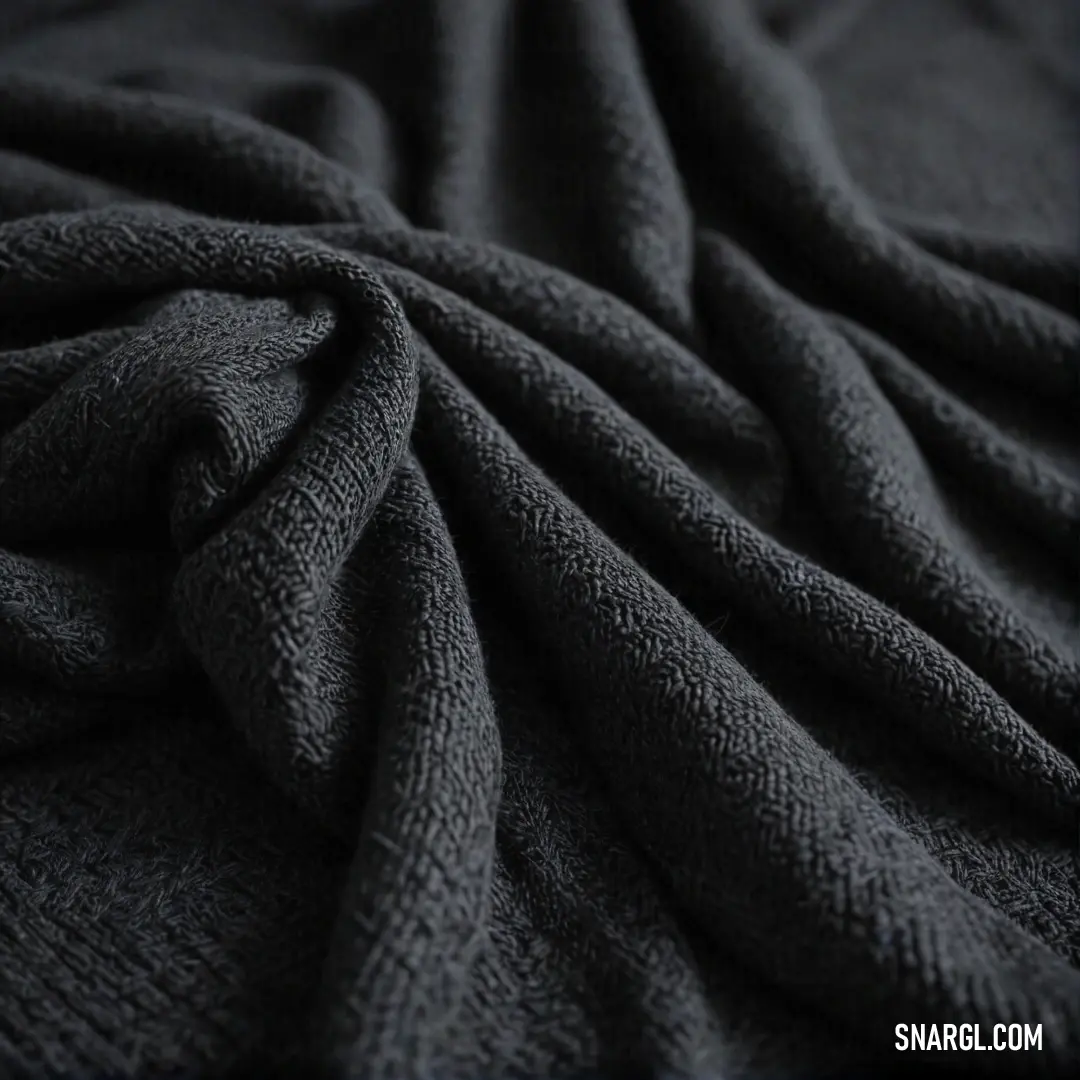 A cozy black blanket, intricately folded on soft bedding, creates a soothing visual against a dark backdrop, emphasizing the deep qualities of PANTONE 519 color in a relaxing environment.