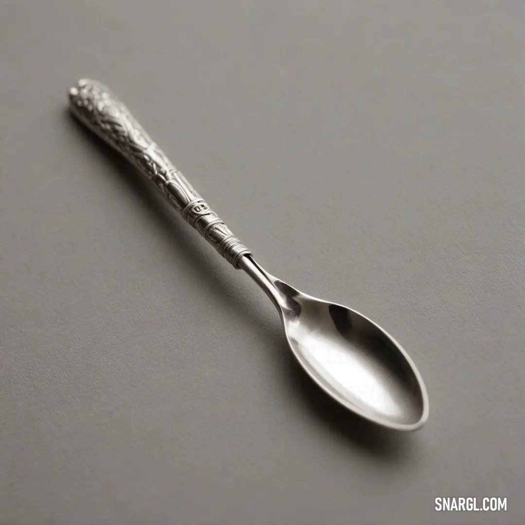 A lone spoon resting elegantly on a table with a gray backdrop, showcasing its polished silver handle. The RGB color profile gives it a chic, contemporary vibe, amplifying its design appeal and making it a feast for the eyes.