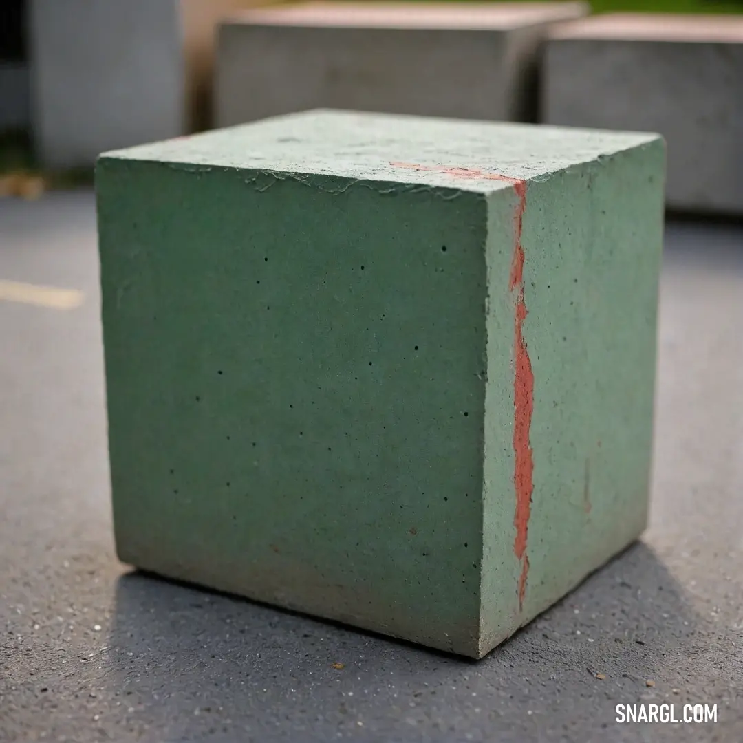 A vibrant scene featuring a square green object adorned with a striking red stripe, sitting gracefully on a textured cement surface. The soft hues of the backdrop enhance the singularity and playful interaction of colors in this captivating composition.