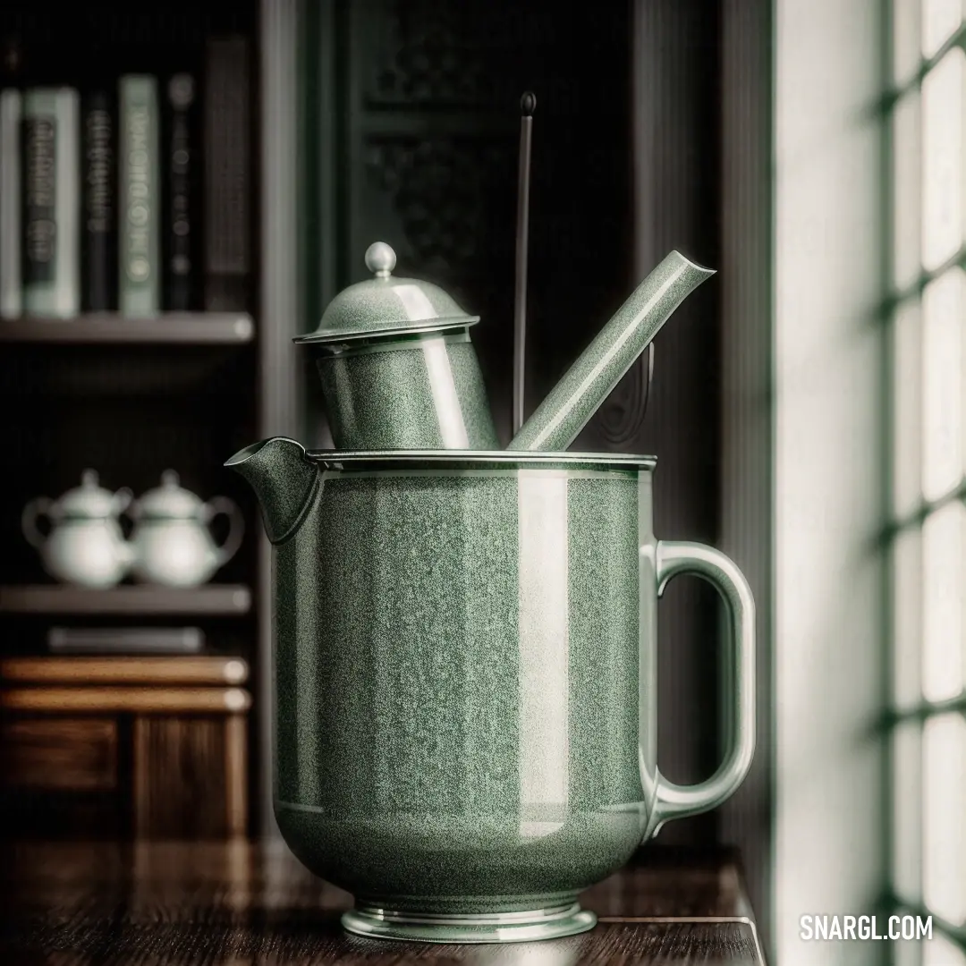 Green tea pot with a tea spoon in it on a table next to a window with bookshelves. Example of #788A7A color.