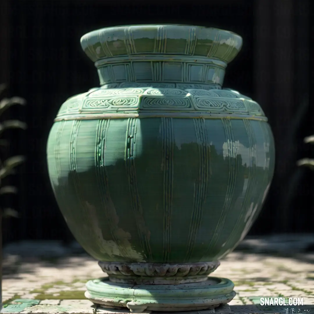 Large green vase on top of a stone floor next to a fence and a building behind it. Example of PANTONE 5635 color.