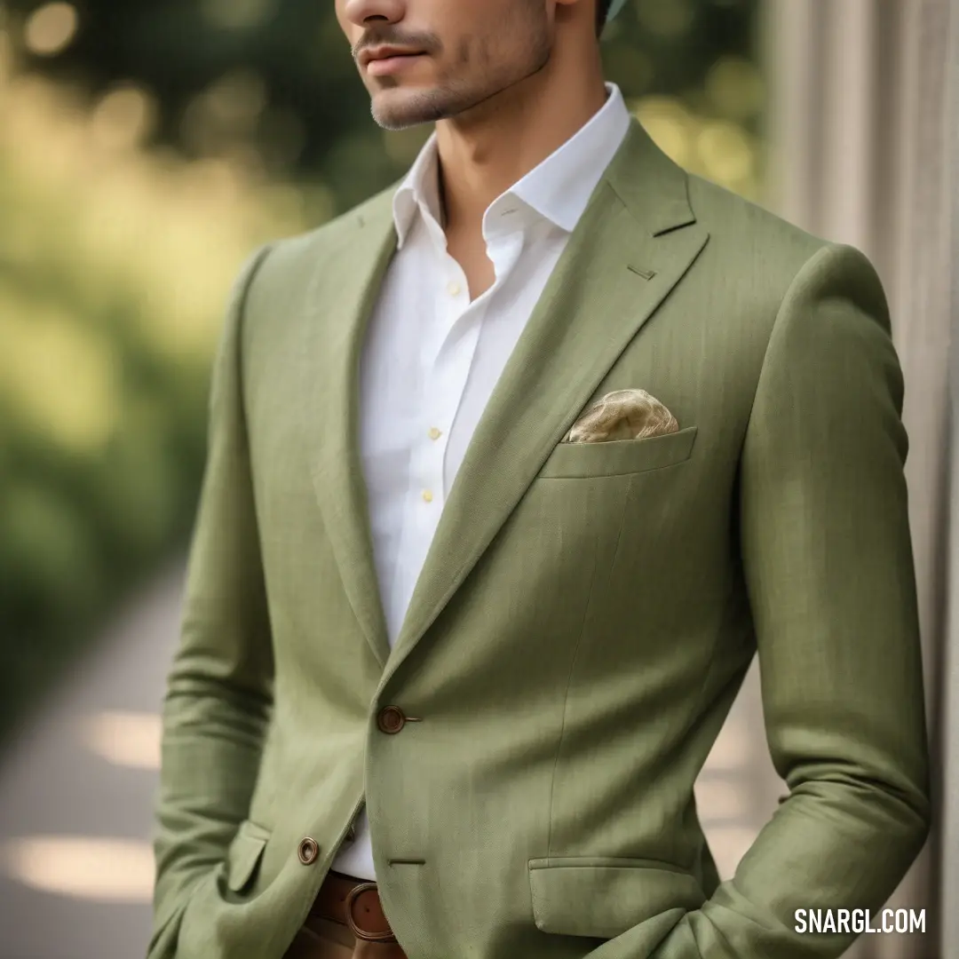 Man in a green suit and white shirt standing next to a wall with his hands in his pockets. Color RGB 139,144,75.