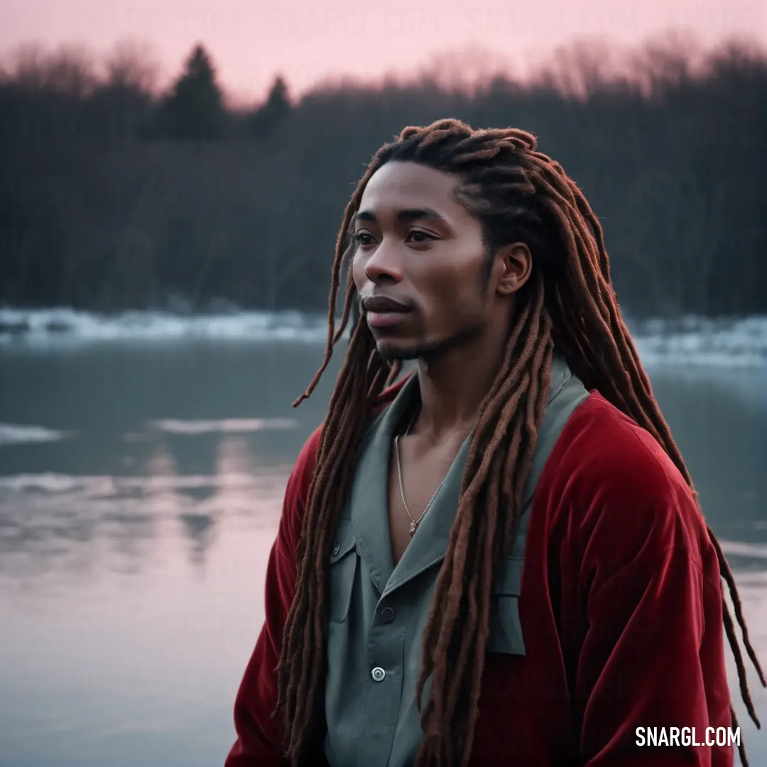 Man with dreadlocks standing in front of a lake at sunset with a pink sky in the background. Color RGB 58,106,88.
