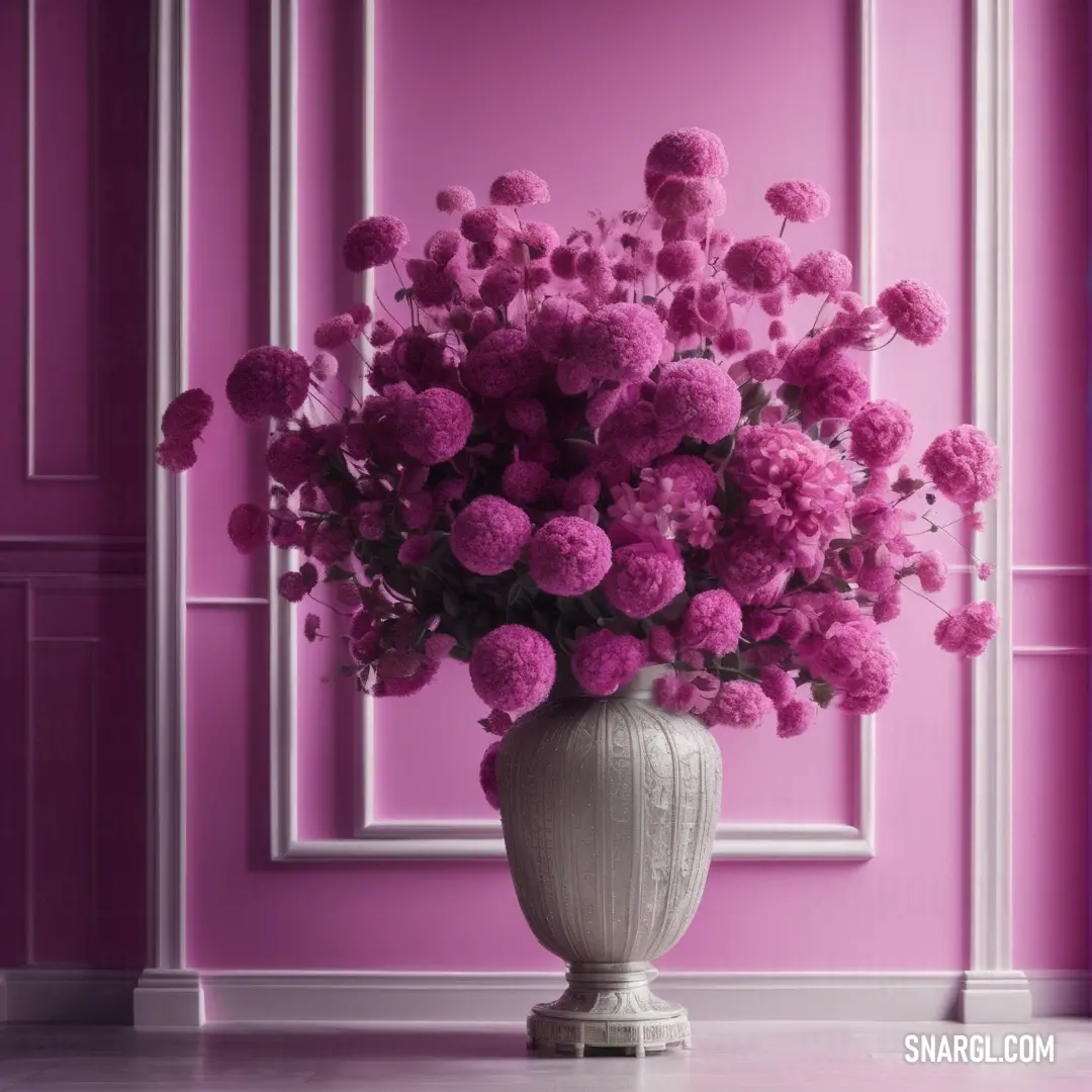 Vase filled with lots of pink flowers on a table next to a wall with a picture frame on it. Color #923C6C.