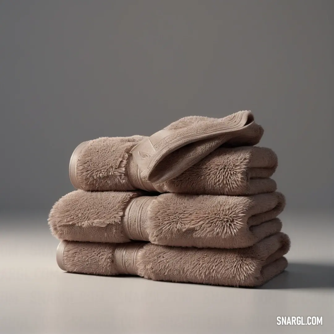 A neatly stacked set of towels arranged on a table, placed side by side with a smooth and serene gray backdrop. The soft textures and subtle hues make the composition both peaceful and organized, with a light touch of color balance.