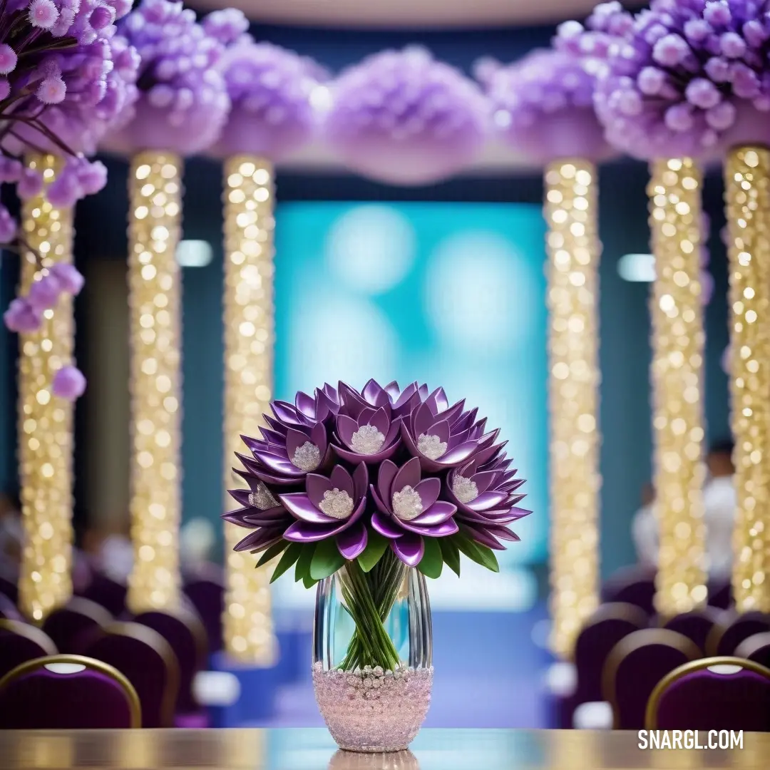 Vase with purple flowers on a table in a room with purple chairs and lights in the background. Example of CMYK 58,87,0,0 color.