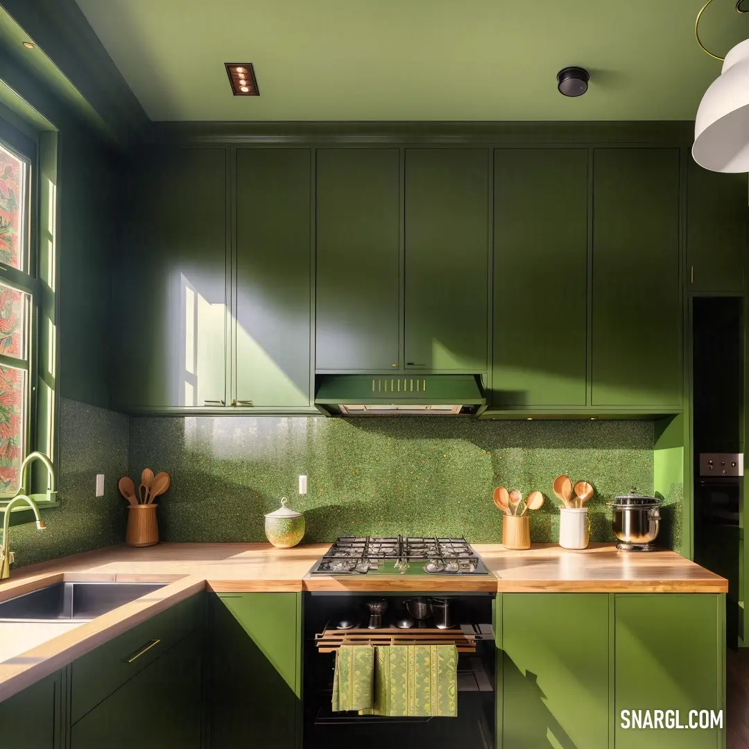 Kitchen with green cabinets and a stove top oven and a sink with a window in the background and a light fixture hanging above