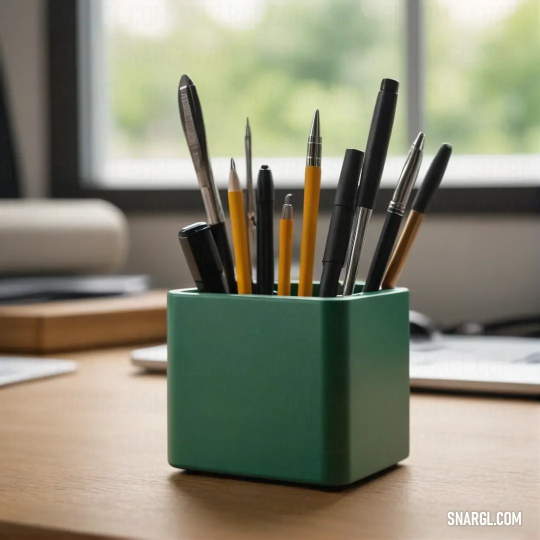 A green container brimming with vibrant pens and pencils adorns a desk, perfectly placed beside a laptop computer and a scenic window. The CMYK representation of 9,83,100,46 adds a playful flair to this functional yet stylish workspace.