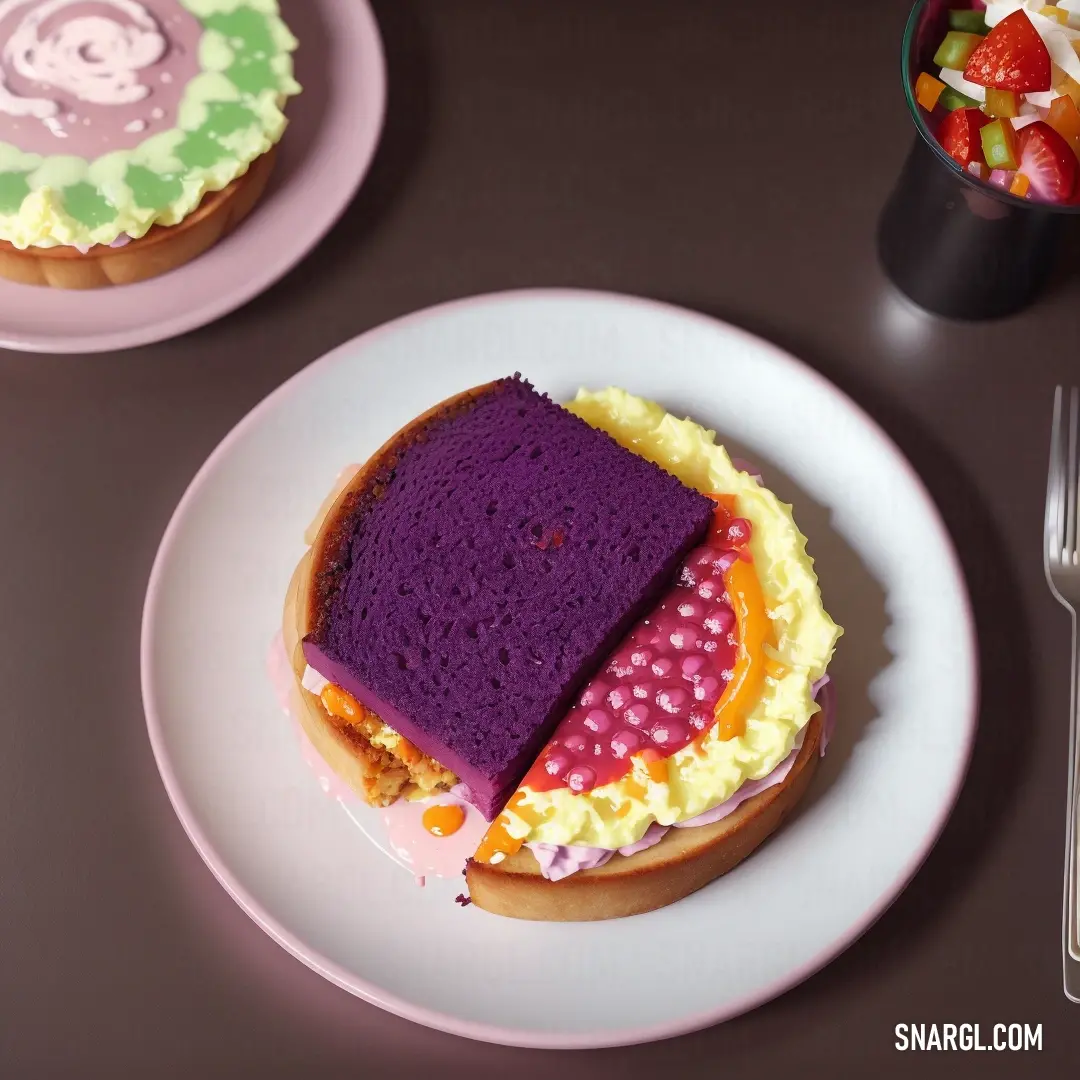 Sandwich with a purple frosting and a pink frosting on it on a plate next to a fork and a cup of fruit. Color PANTONE 7652.