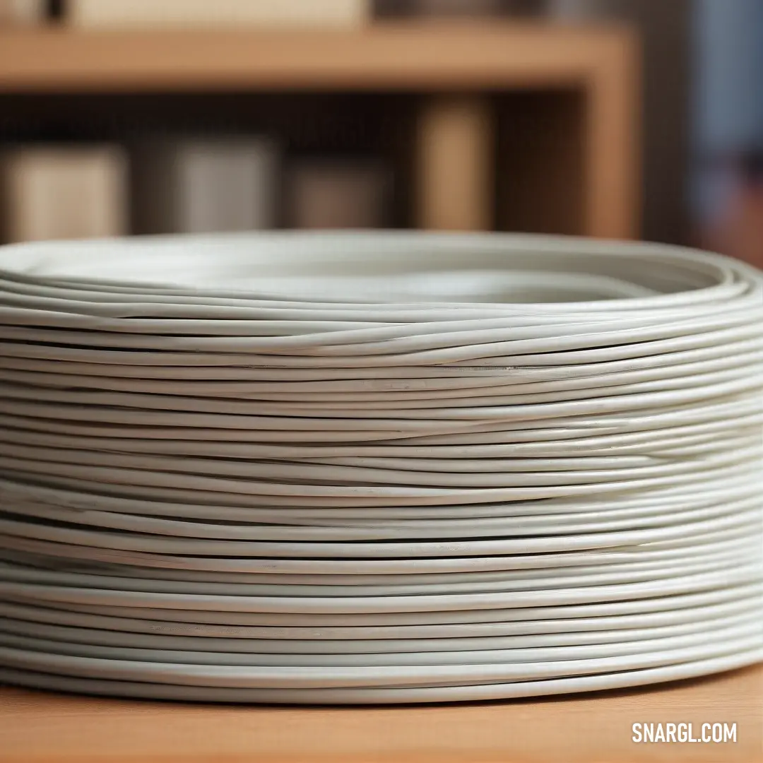 Stacked with care, a collection of pristine white plates is artfully arranged on a rustic wooden table, creating a charming contrast. In the background, a bookcase filled with books hints at cozy moments spent enjoying meals and stories intertwined.