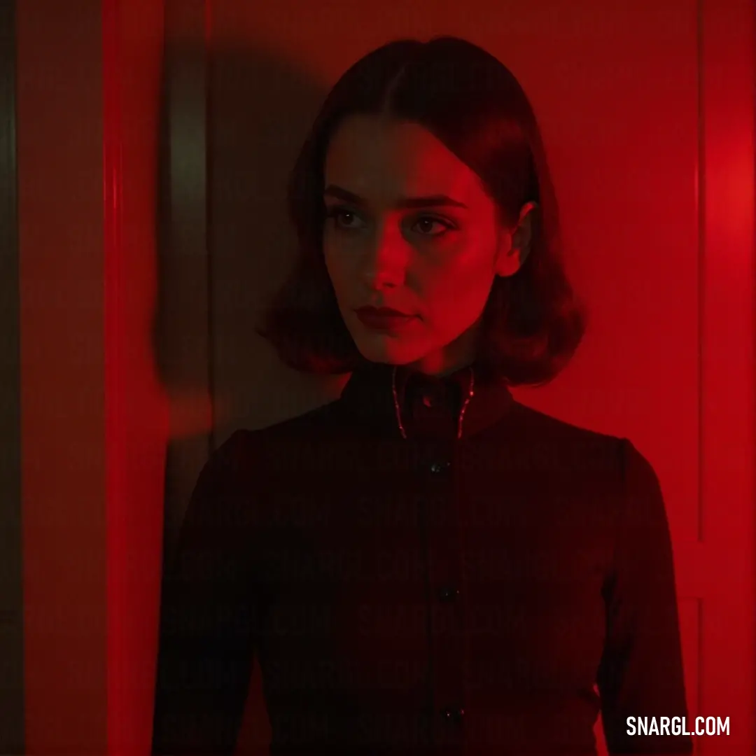 A woman dressed in a sleek black shirt stands confidently in a vividly colored red room. The warm red light casts dramatic shadows on her face, transforming her look into a striking visual experience surrounded by an ambiance of intrigue and intensity.