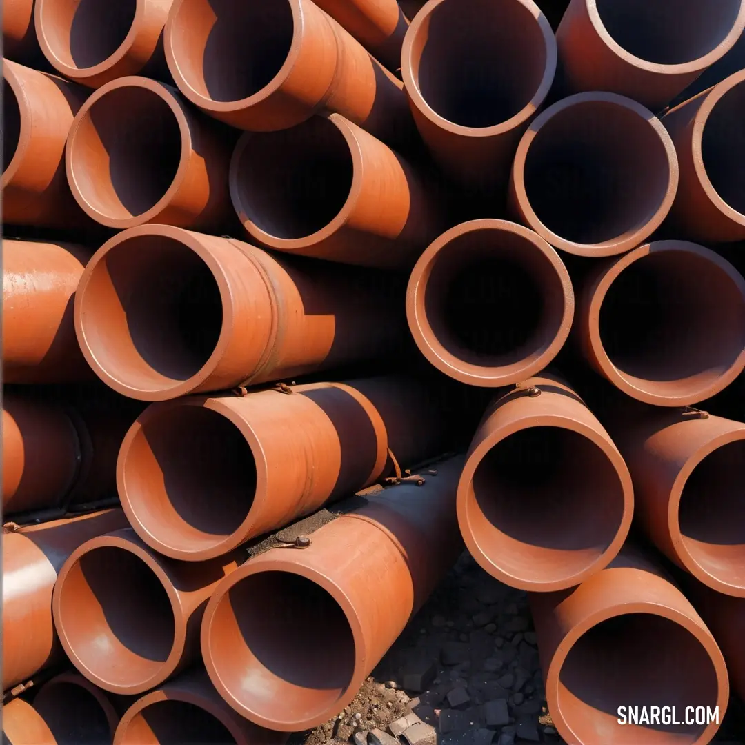 A pile of orange pipes stacked atop each other creates a vibrant display of industrial beauty. Set against a rugged backdrop of gravel and rocks, this scene highlights the raw complexity of materials, inviting an appreciation for structural artistry.