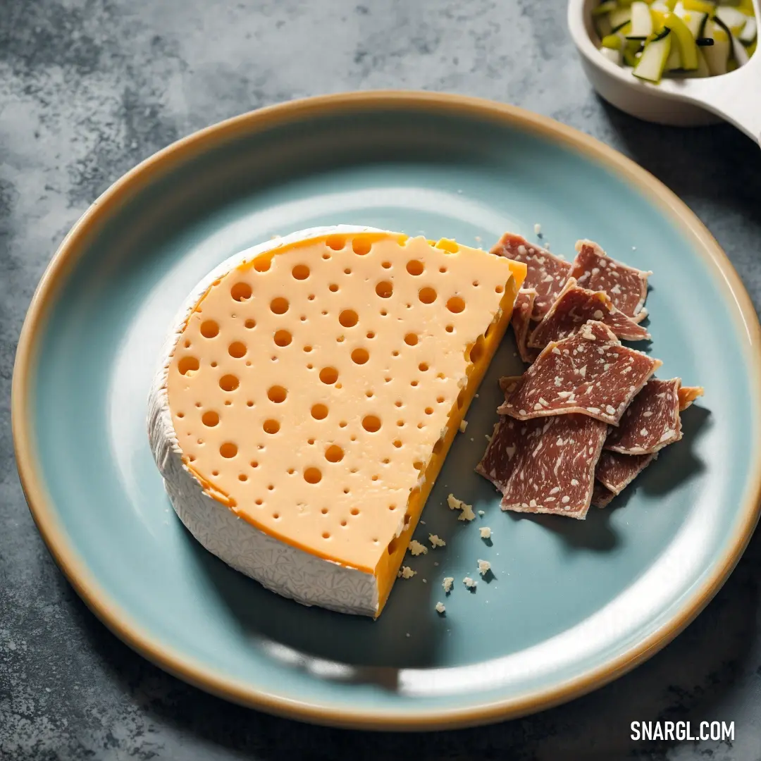 Plate with a piece of cheese and crackers on it next to a bowl of pickles