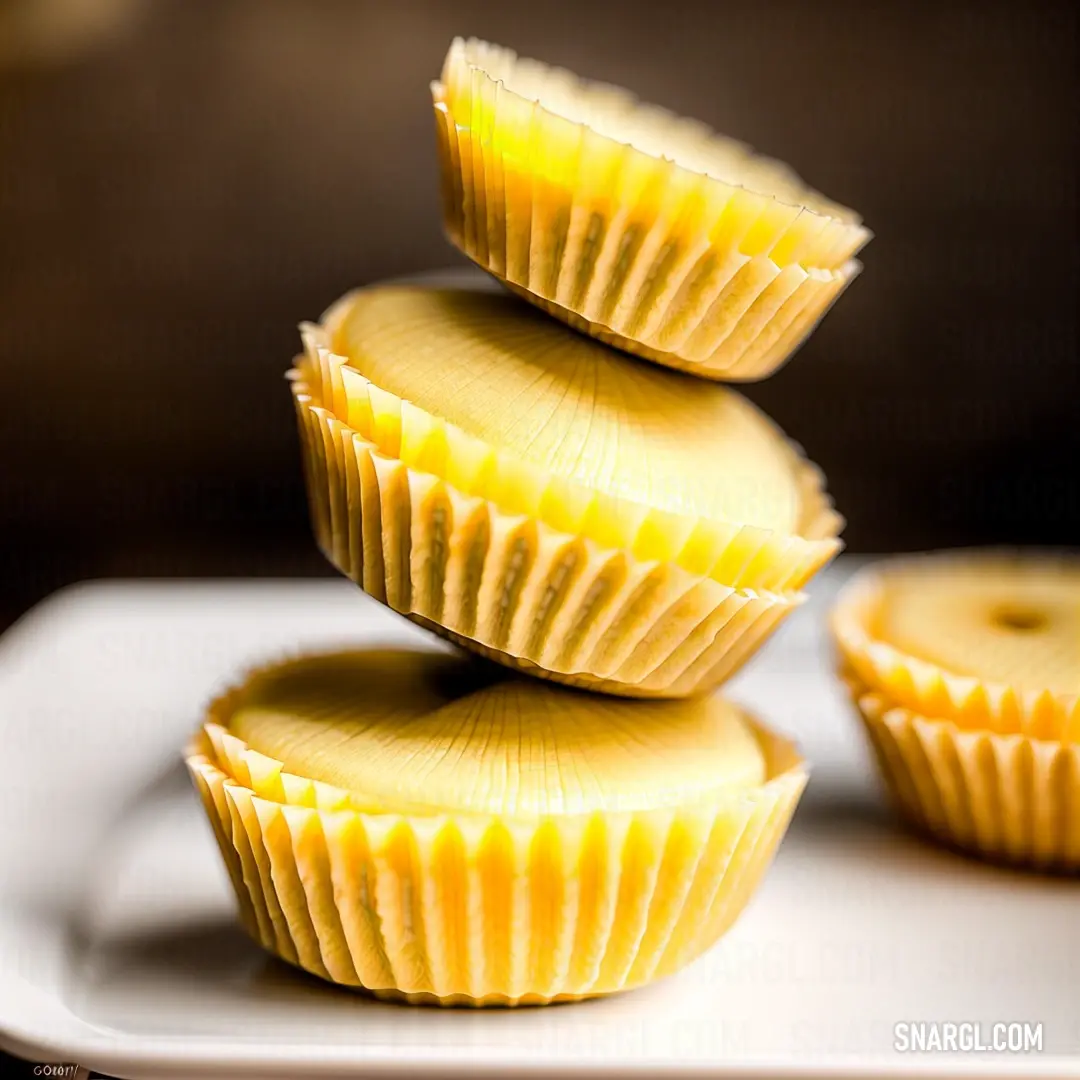 White plate topped with three yellow cupcakes on top of each other on a table next to a brown wall