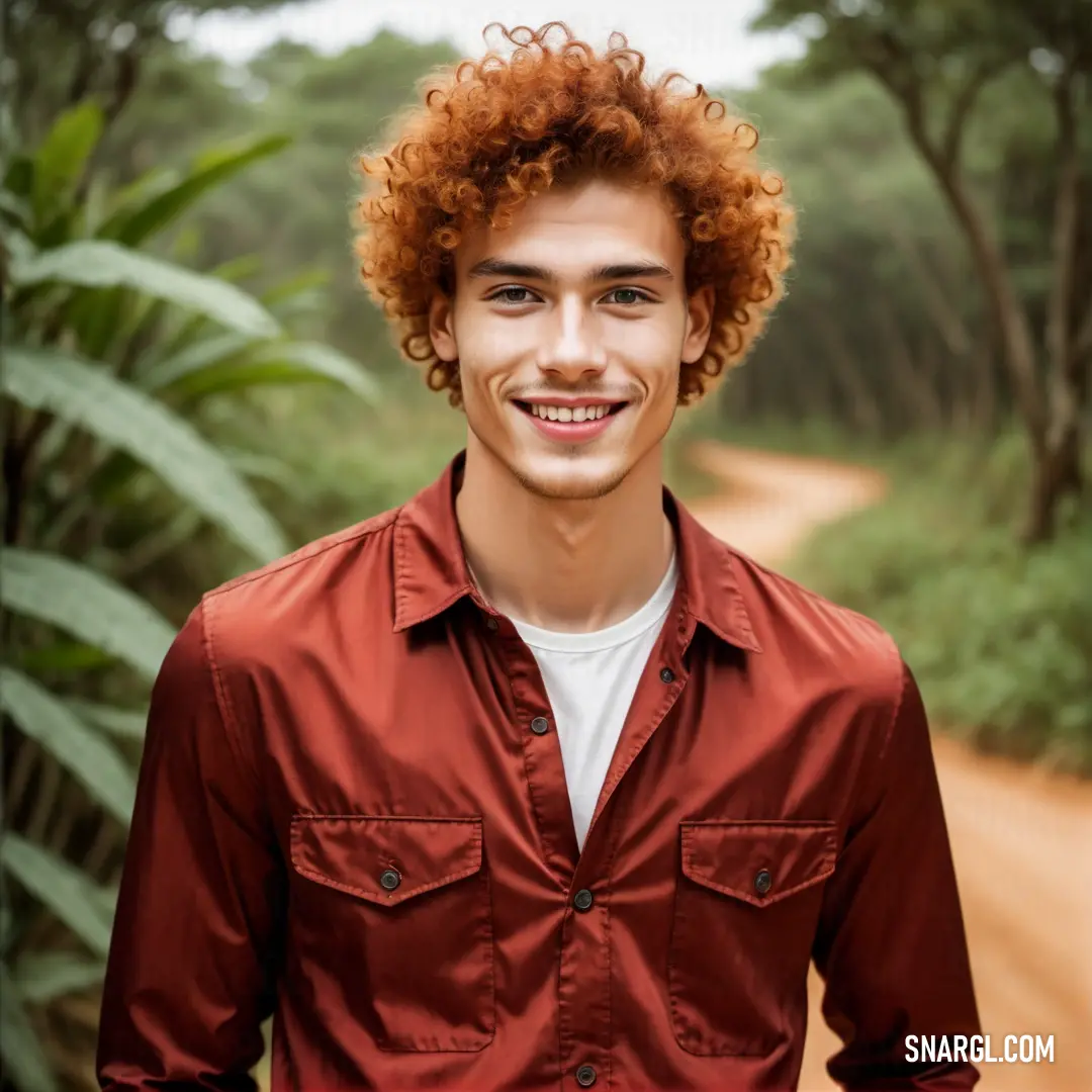 Man with red hair and a smile on his face standing in front of a dirt road in the jungle