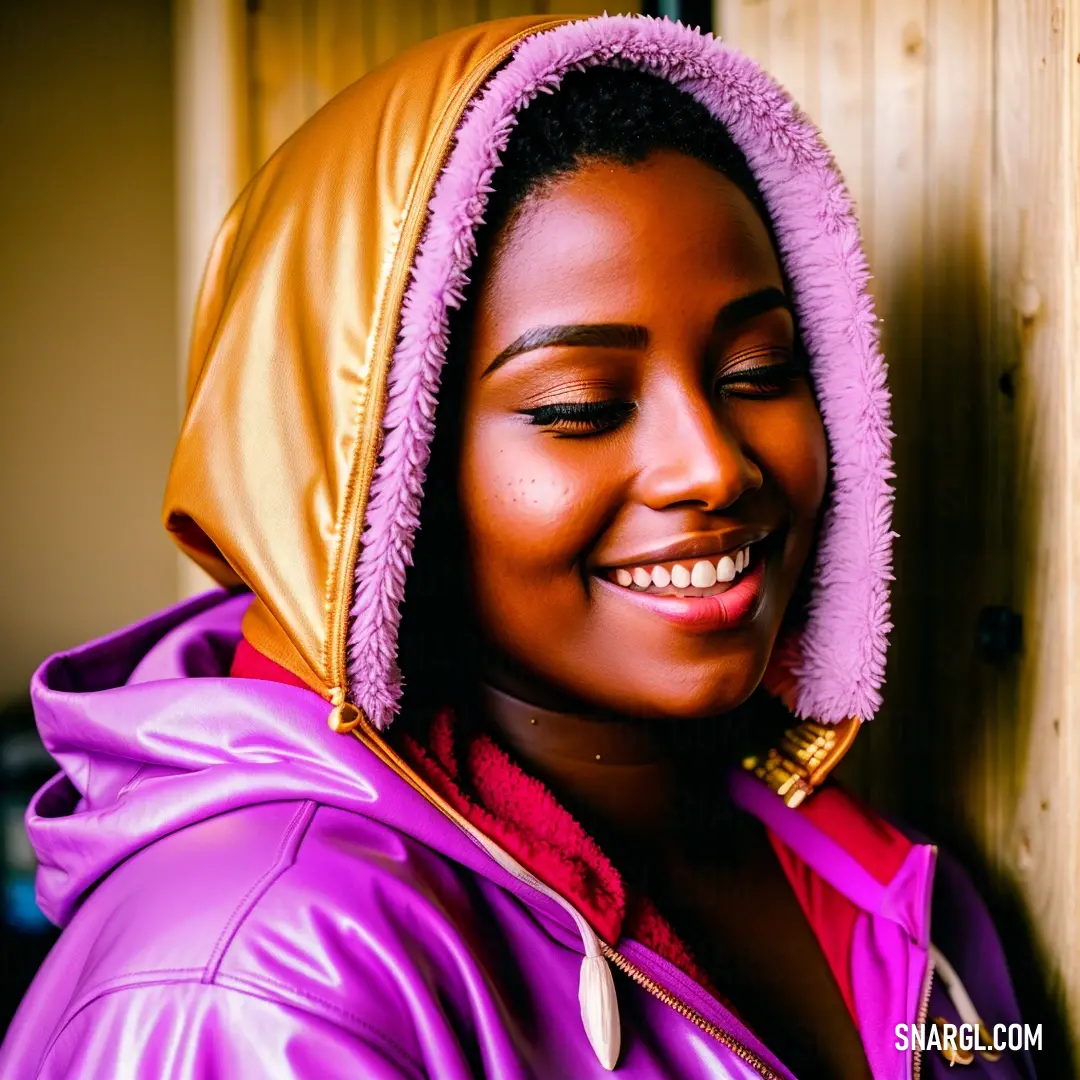 Woman in a purple jacket smiling and wearing a hoodie over her head and a wooden door behind her