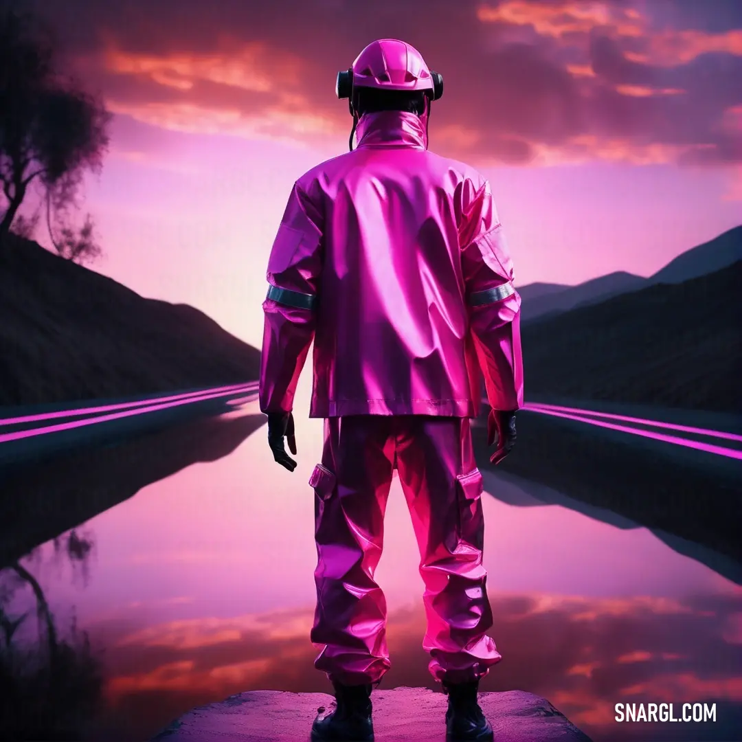 Man in a pink suit standing on a dock looking at a lake at sunset with mountains in the background. Color RGB 252,116,253.
