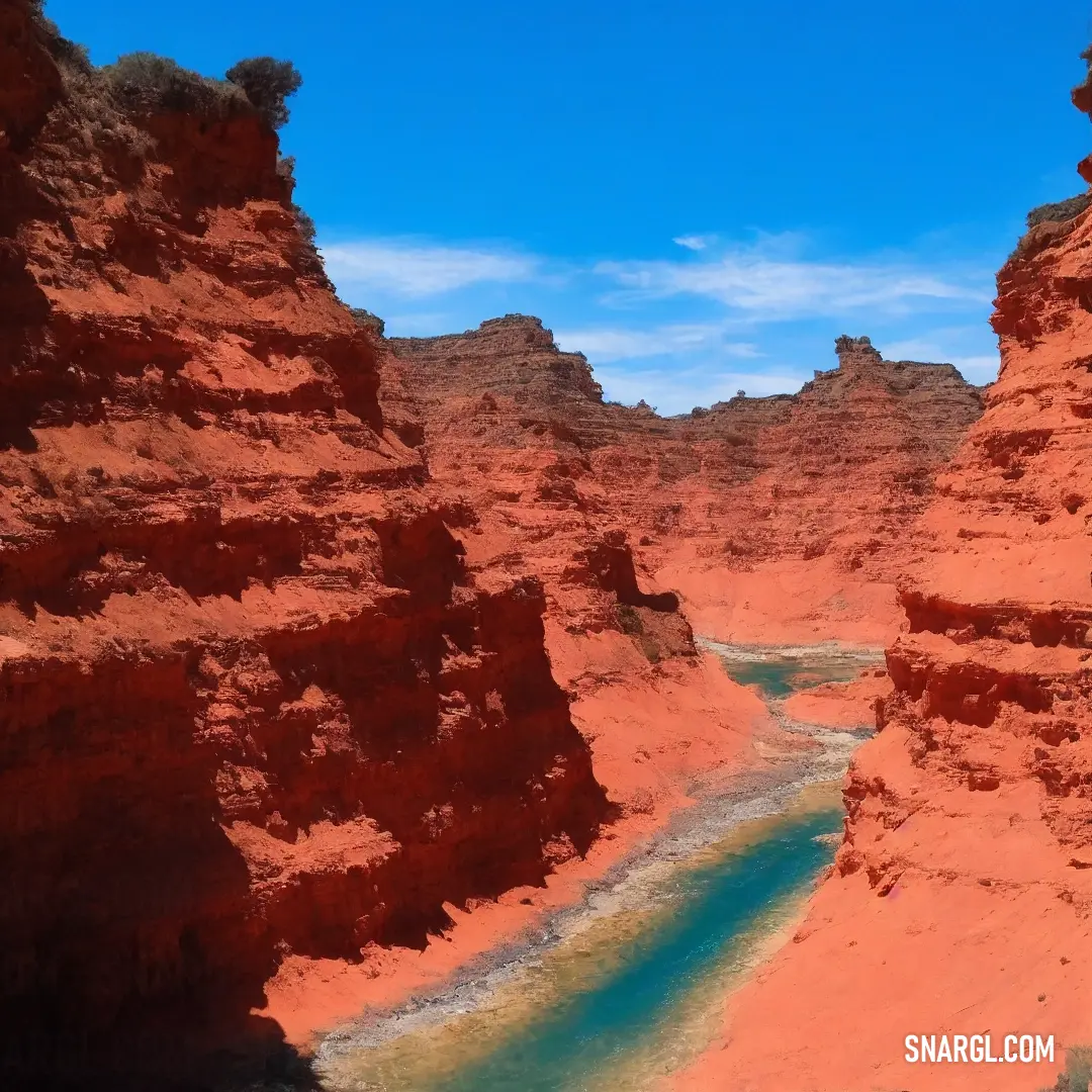 River in a canyon with red rocks and water in it and a blue sky above it with a few clouds